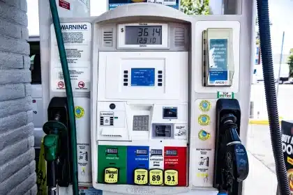 Mano che inserisce la pistola del carburante in un distributore di gasolio, con display dei prezzi sullo sfondo