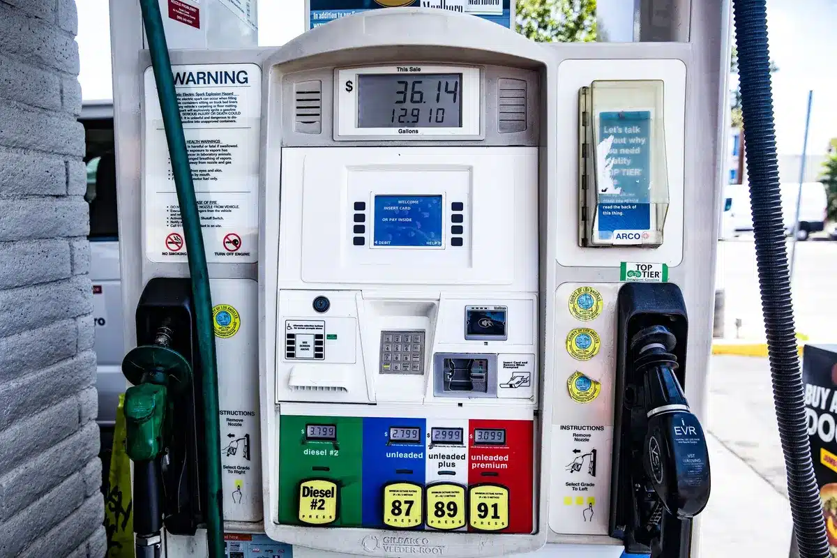 Mano che inserisce la pistola del carburante in un distributore di gasolio, con display dei prezzi sullo sfondo