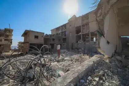Strada distrutta con macerie, operatori di emergenza e civili tra le rovine di edifici danneggiati