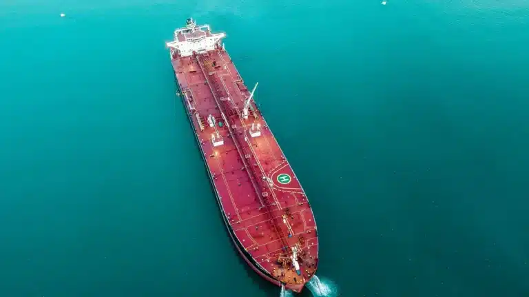 Petroliera in transito in uno stretto con navi militari sullo sfondo e terminali petroliferi costieri visibili
