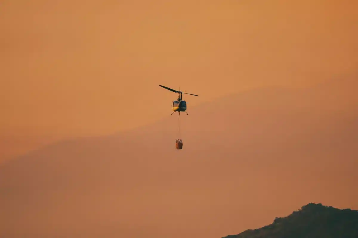 Elicottero antincendio in azione sopra un incendio boschivo con squadre di emergenza a terra