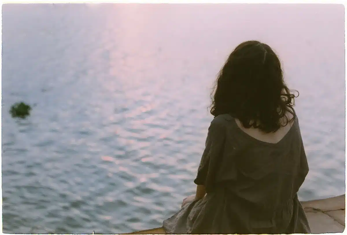 Una donna sola riflette accanto all'acqua, in un momento di crisi e riflessione interiore.