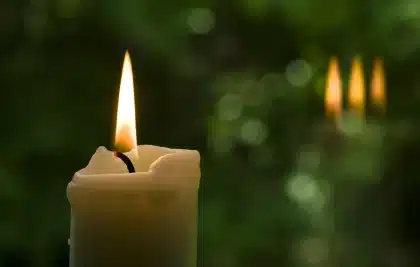 Folla anonima davanti a una chiesa con candele e bandiere, vista di schiena