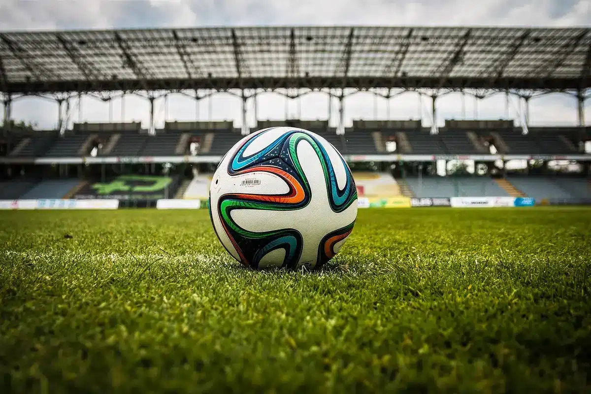 Scarpe da calcio generiche e palla su erba artificiale davanti a un tunnel di stadio