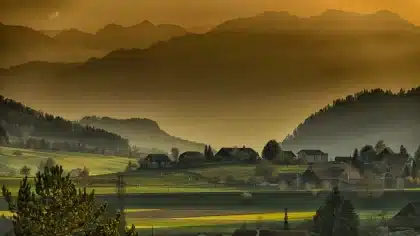 Paesaggio autunnale di un piccolo borgo costiero con alberi spogli e mare grigio sotto cielo nuvoloso.