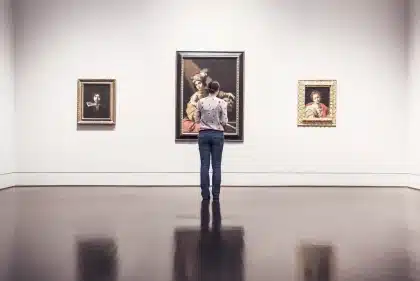 Mani anonime che sistemano una scultura in una sala espositiva con cataloghi