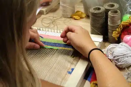 Mani anonime al telaio tessile con una mappa della città sul tavolo