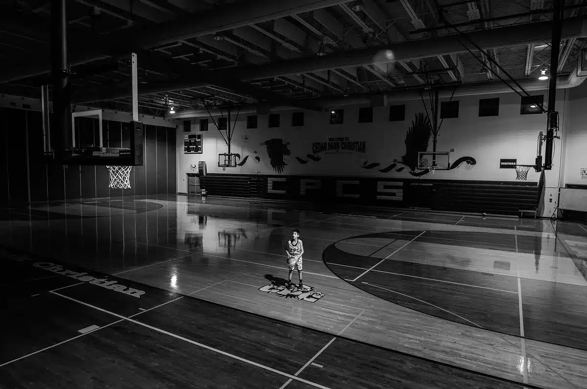 Mani in silhouette che applaudono vicino a una palla da basket su un parquet di arena